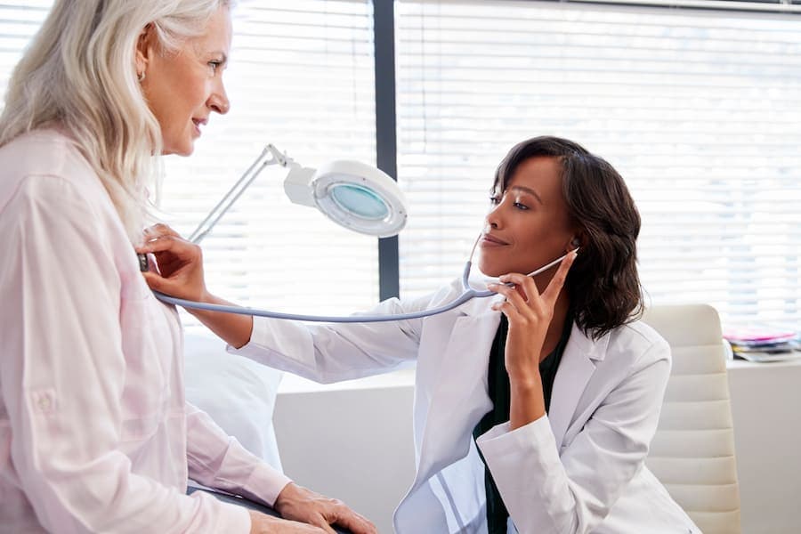 Médica examina paciente mulher com estetoscópio
