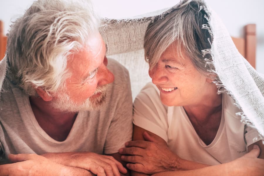 Casal de idosos sorriem um para o outro embaixo de um lençol