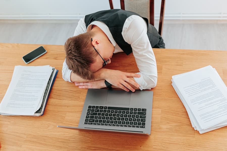 homem dorme na mesa do escritório , próximo ao notebook