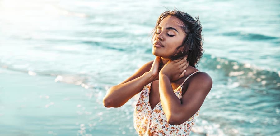 jovem mulher com as mãos nos cabelos e o mar ao fundo