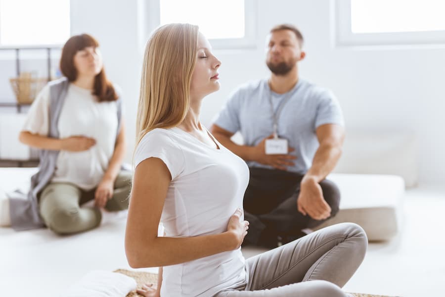 Duas mulheres e um homem sentados fazem exercícios de respiração