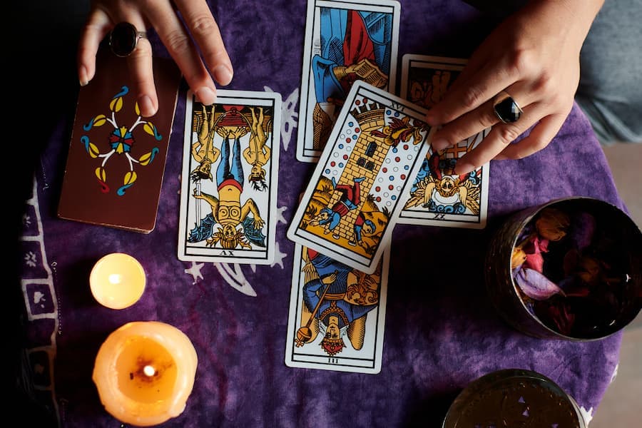 mãos de mulher abre cartas de tarô sobre mesa com toalha rocha e velas acesas