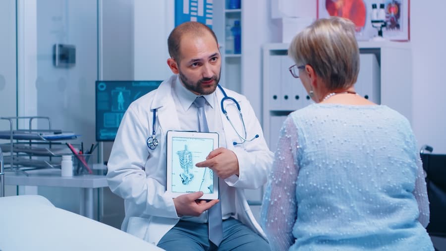 Médico com tablet com imagem de esqueleto, atende senhora idosa