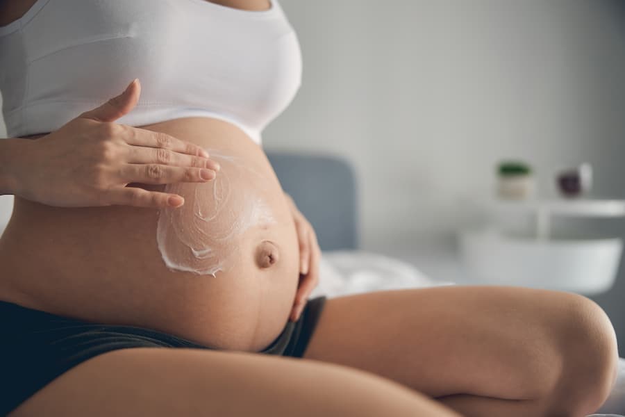 barriga de mulher grávida, mãos passando creme