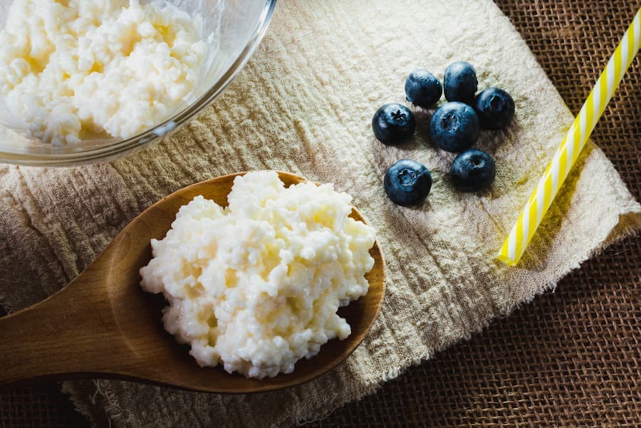 tigela e colher de pau com grãos de kefir e um canudo plástico