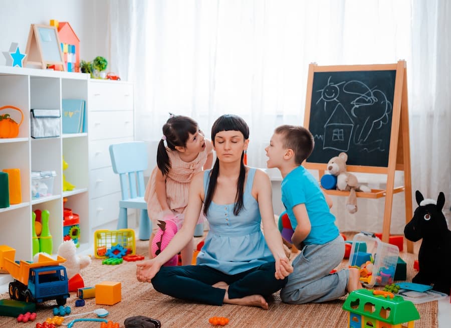 mãe tenta fazer ioga, com uma criança de cada lado pedindo atenção e gritando