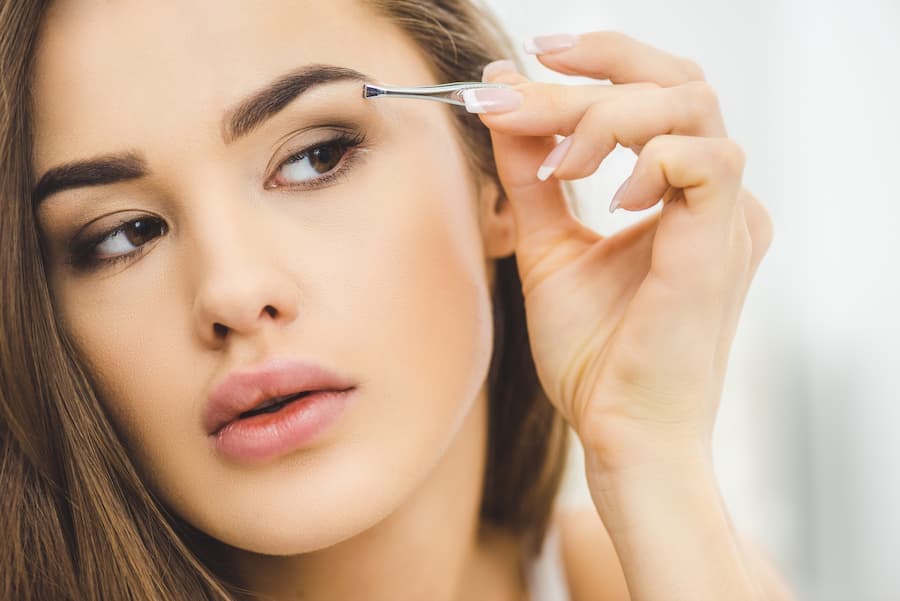 Mulher tira sobrancelhas com a pinça