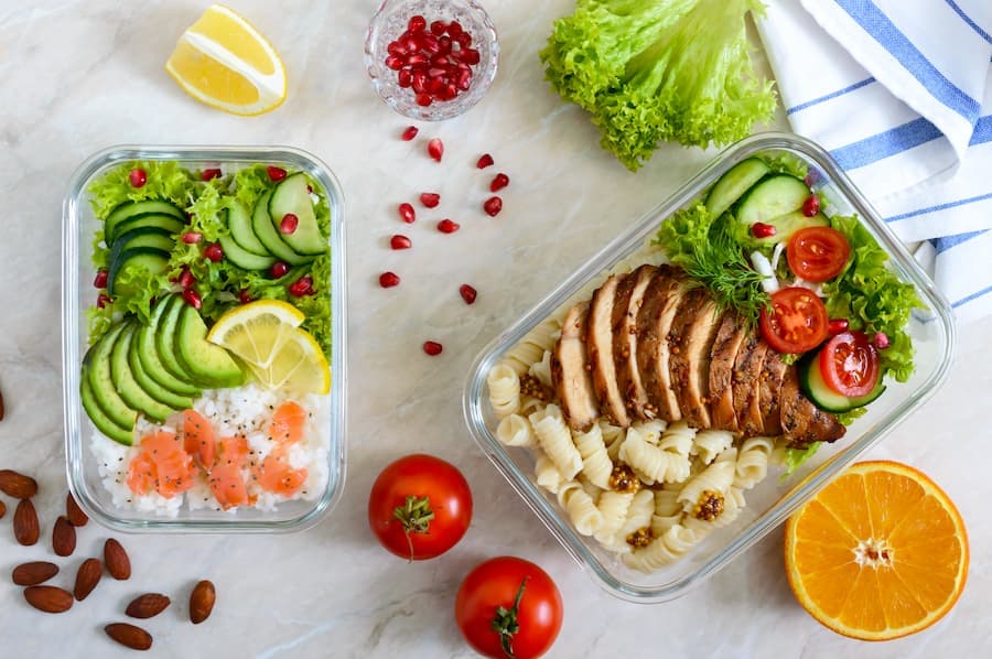 duas marmitas sobre uma mesa - uma contem arros peixes e legumes a outra carne assada, massa e salada