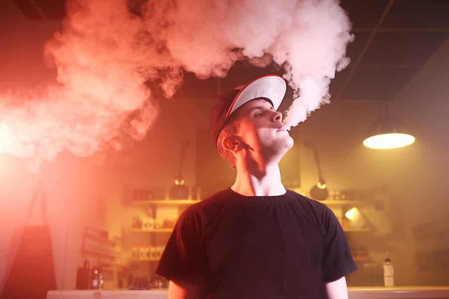 Homem jovem solta fumaça do dispositivo vape