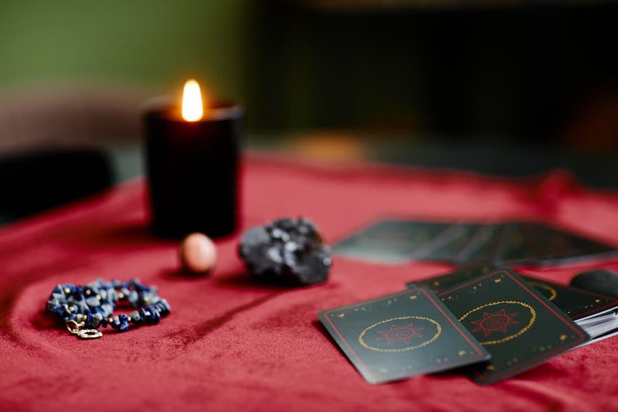 mesa com toalha vermelha, vela acesa, cartas e cristais