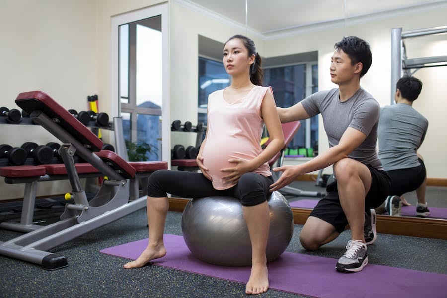 mulher oriental grávida faz exercícios com auxilio de treinador
