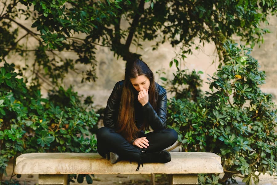 Jovem mulher sentada em um banco de praça, pensativa