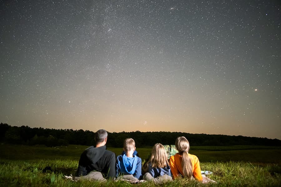 Família - pai mãe e duas crianças - deitada na relva, em campo aberto, à noite contemplando as estrelas