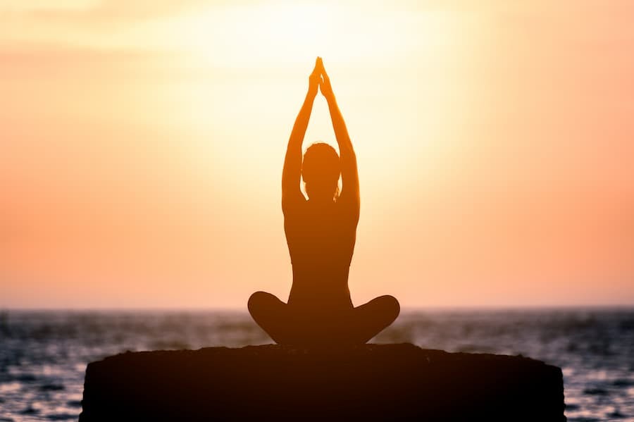 Silhueta de mulher sentada fazendo ioga ao por do sol