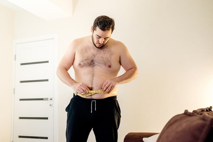 Homem sem camisa mede a cricunferência da barriga com uma fita métrica