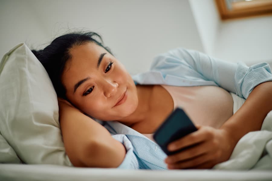Jovem mulher deitada na cama mexendo no celular