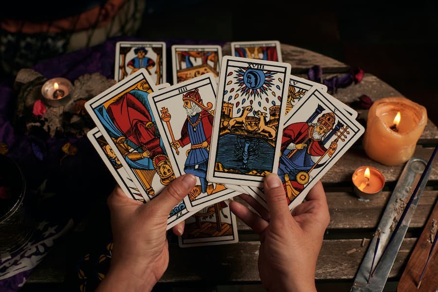 mão de mulher segura cartas de tarô com vela acesa e incenso ao lado