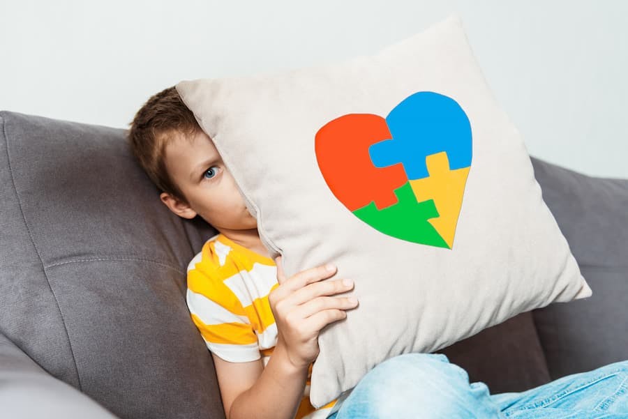 menino segura almofada com símbolo do autismo - coração colorido imita quebra-cabeça