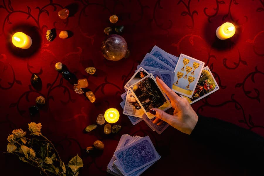 mesa com toalha vermelha, cristais, velas mãos de mulher seguram baralho de tarô