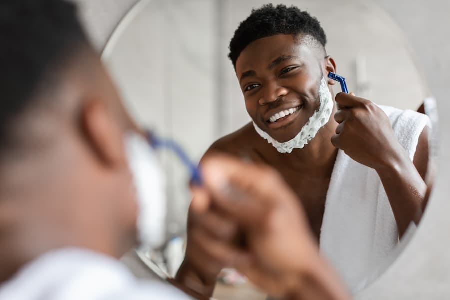 Jovem negro faz a barba em frente ao espelho
