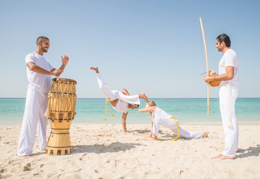 Grupo de pessoas pratica capoeira na praia