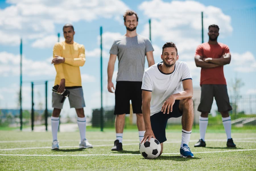 quatro homens fazem pose com a bola para foto, num campo de futebol