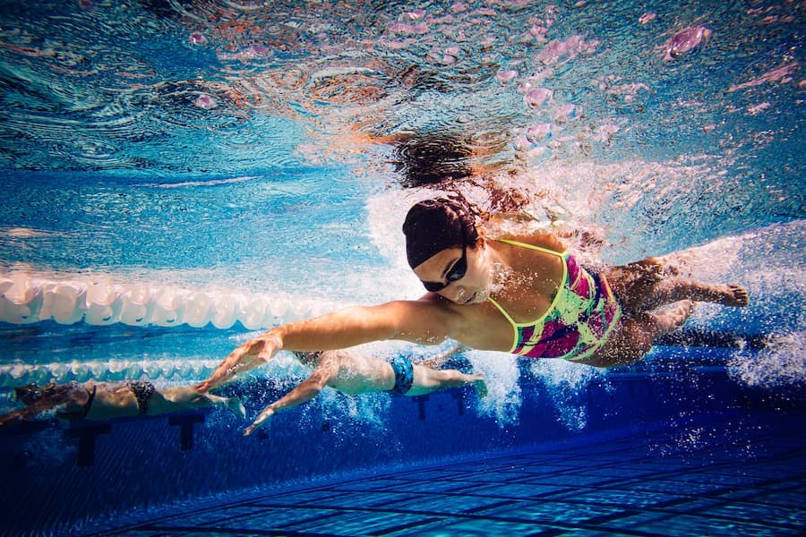 Nadadores na piscina, mulher à frente, vistos por debaixo da água