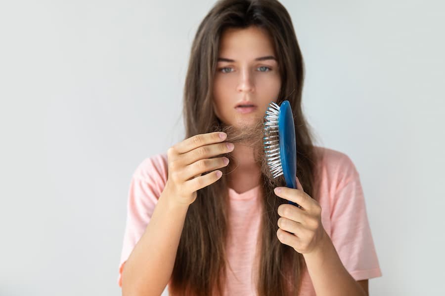 Mulher jovem de cabelos compridos se assusta com tufos de cabelos na escova