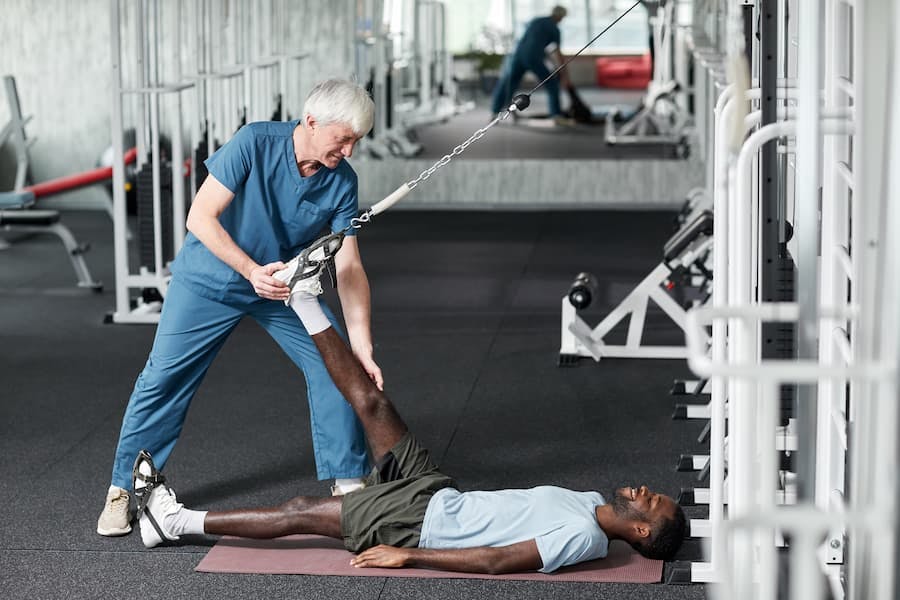 Homem de meia idade, fisioterapeuta, auxilia rapaz em exercício