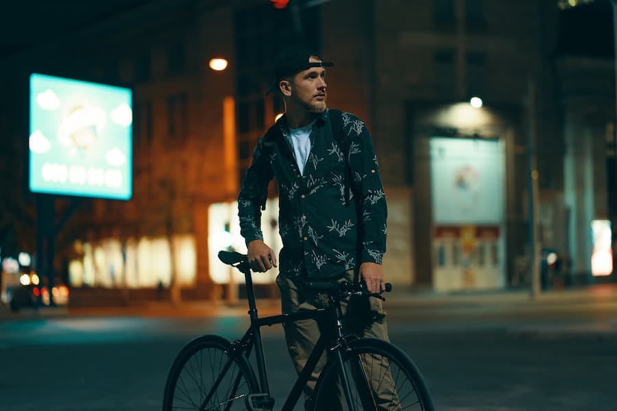 Rapaz ciclista noturno parado ao lado da bicicleta
