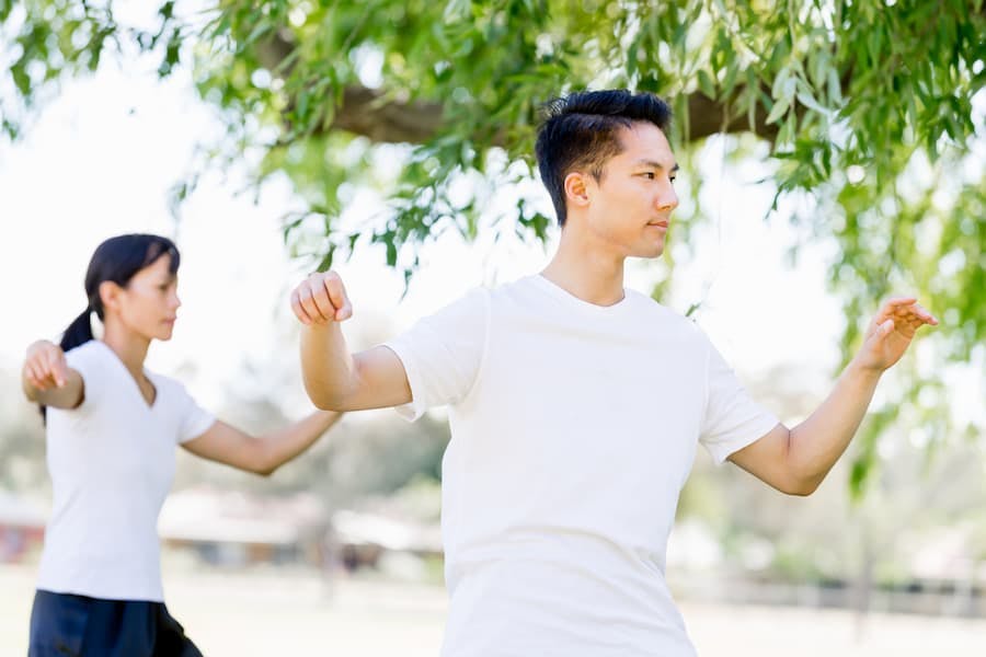 Homem e mulher, jovens, praticam lian gong ao ar livre