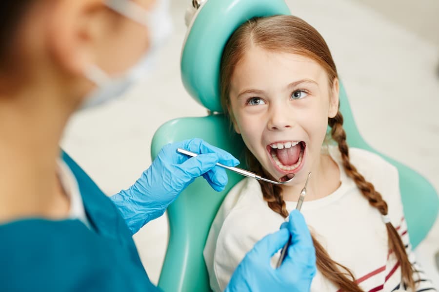 Menina tem a boca examinada por dentista